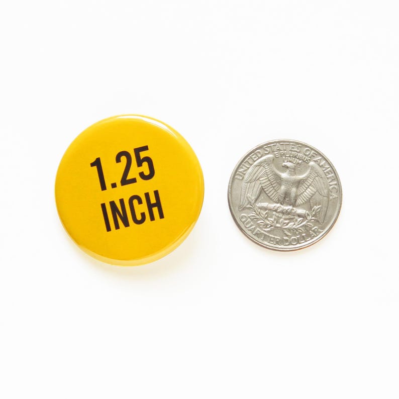 Round yellow pinback button that reads 1.25 Inch in black text. Pinback button is next to a Quarter coin for size comparison.