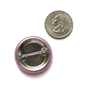 back of a metal pinback button next to a quarter for size comparison