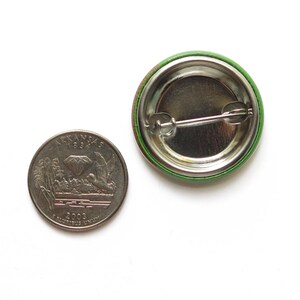 Back of a metal pinback button next to a quarter coin.