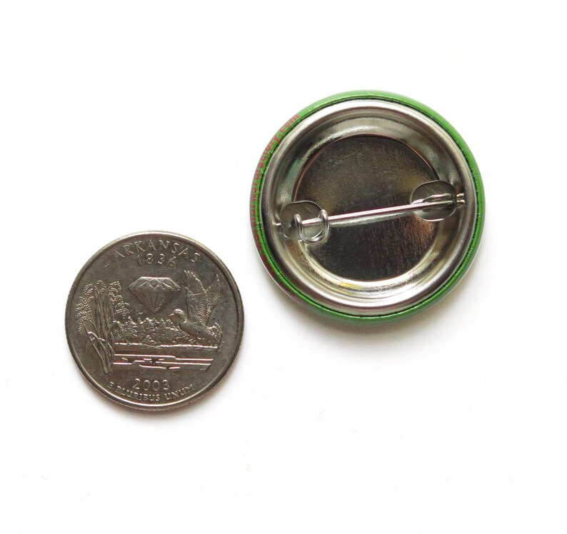 Back of a metal pinback button next to a quarter coin.
