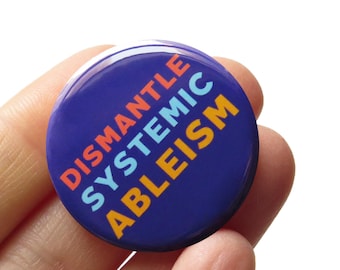 Op de afbeelding: Een blauwe knop met de woorden "Dismantle Systemic Ableism" in oranje, roze en blauwe letters.