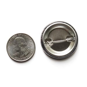 back of a round pinback button, next to a quarter coin for size reference.