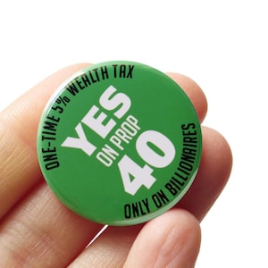 May include: A round green pin-back button featuring white and black text that reads YES ON PROP 40, ONE-TIME 5% WEALTH TAX, and ONLY ON BILLIONAIRES. The button has a glossy finish and is circular in shape with bold, high-contrast lettering.