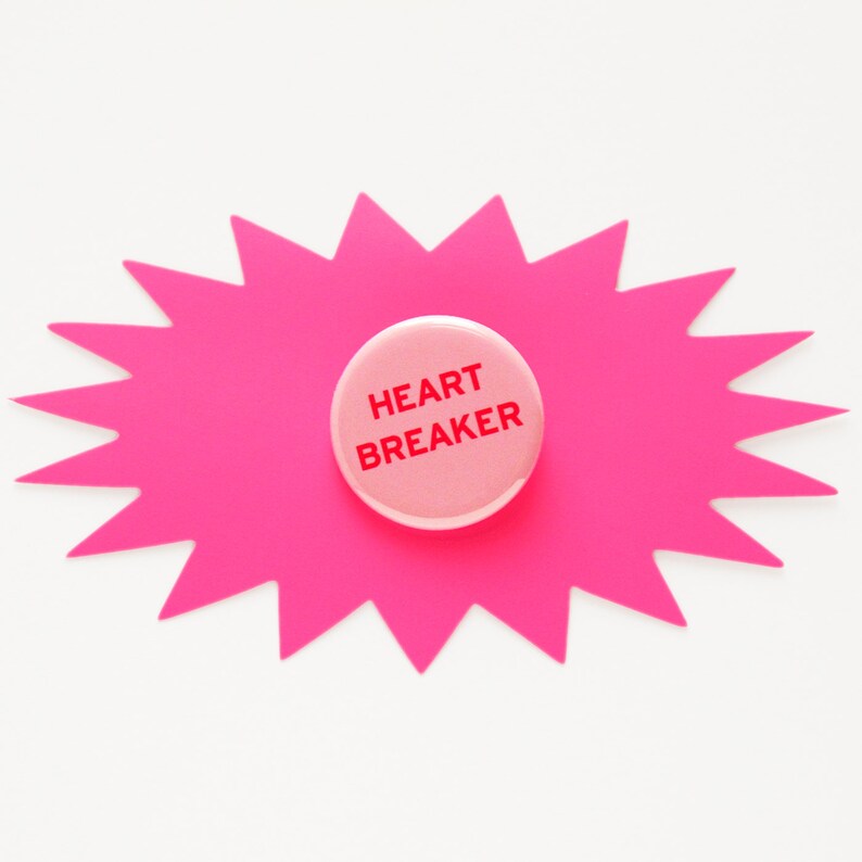 May include: Pink starburst shaped paper with a pink button in the center. The button has the text "HEART BREAKER" in red.