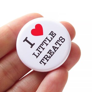 Peut inclure: Bouton blanc avec un cœur rouge et le texte "J'aime les petites gâteries" en noir.