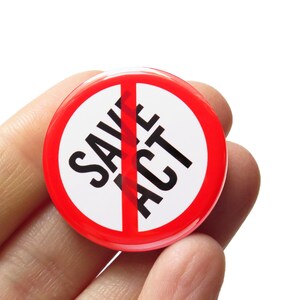 Peut inclure: Un bouton rond rouge et blanc avec les mots "SAVE ACT" en noir, barrés d'une ligne rouge. Le bouton est tenu dans une main sur fond blanc.