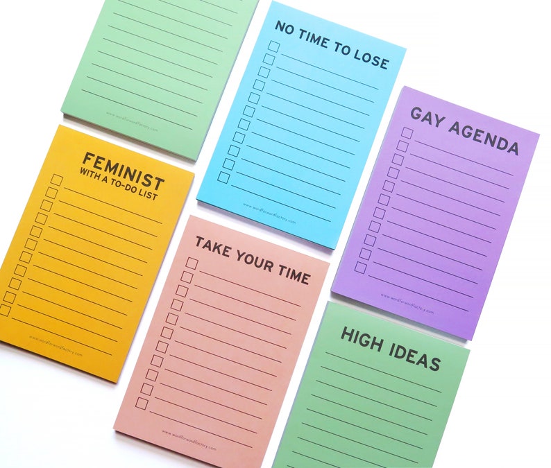 Four vertical rectangle notepads with boxes & lines that read GAY AGENDA, HIGH IDEAS, NO TIME TO LOSE, TAKE YOU TIME & FEMINIST WITH A TO-DO LIST. In lavender, goldenrod, teach, light green & light blue.