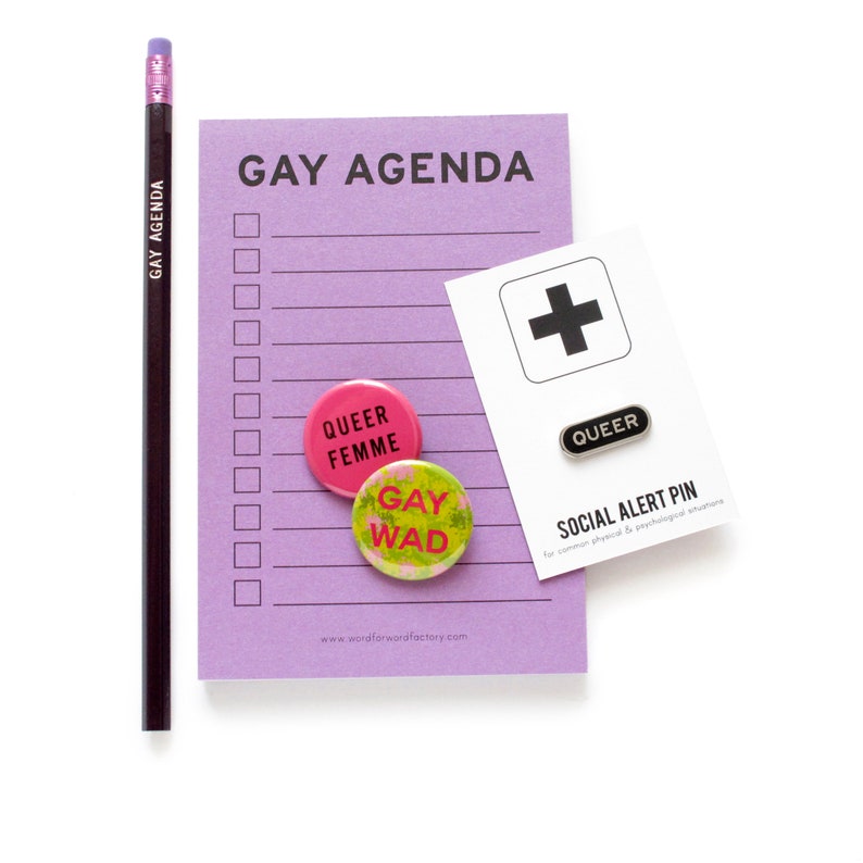 A vertical rectangle lavender notepad that reads GAY AGENDA at the top, with 11 check boxes and lines for list making. A matching pencil, Queer Femme & Gay Wad Buttons & a Queer Enamel Pin.