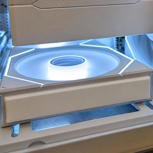 Op de afbeelding: Een witte computerkoelventilator met geïntegreerde ledverlichting, voorzien van een vierkant frame en een ronde centrale naaf. De ventilator is gemonteerd in een witte computerbehuizing en heeft een strakke, heldere uitstraling.