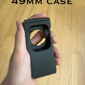 May include: A black 49mm case is held in a hand. The case has a rectangular shape with a circular opening. The text "49MM CASE" is displayed above the case.