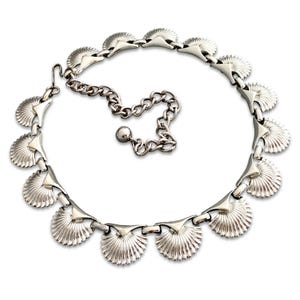 May include: A silver-toned necklace featuring a series of fan-shaped pendants. The necklace has a chain extension for adjustable sizing and a hook clasp. The design is symmetrical, with each fan-shaped element connected by small links.