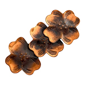 May include: Three copper-colored flower-shaped metal embellishments. Each flower has four petals with etched lines and a central cluster of small dots. The metal has a distressed finish with darker areas, giving it an aged appearance.