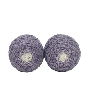 May include: Two balls of purple yarn with a white center. The yarn is wound into a ball shape.
