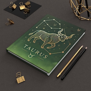 Könnte beinhalten: Grünes Notizbuch mit einer goldenen Illustration des Sternzeichen Stier und seiner Konstellation. Der Text "TAURUS" ist in goldenen Buchstaben geschrieben.