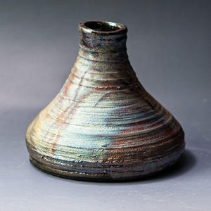 May include: A small, ceramic vase with a wide, flared base and a narrow neck. The vase is decorated with a swirling, iridescent glaze in shades of blue, brown, and white.