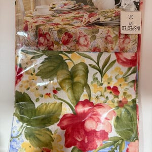 May include: A floral tablecloth and matching napkins, packaged in plastic. The tablecloth features a pattern of red, pink, and yellow flowers with green leaves. The packaging reads "Simply Carefree" and "Summer Ballad".