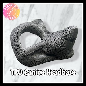 Könnte beinhalten: Eine schwarze, 3D-gedruckte TPU-Hundekopfbasis mit texturierter Oberfläche, ausgeprägter Schnauze und einer großen kreisförmigen Augenöffnung. Das Objekt trägt den Text StarburstwrksEtsy an der Unterseite und ist als TPU Canine Headbase beschriftet.