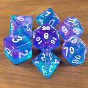 May include: A collection of seven multi-sided dice in blue and purple hues, each with white numerals. The dice have a translucent, marbled appearance, resembling a galaxy. Ideal for role-playing games.