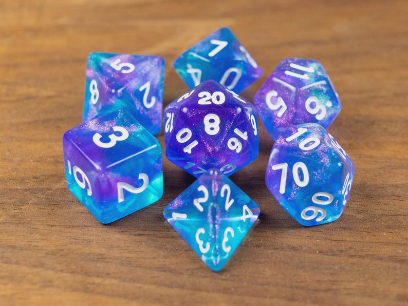May include: A collection of seven multi-sided dice in blue and purple hues, each with white numerals. The dice have a translucent, marbled appearance, resembling a galaxy. Ideal for role-playing games.