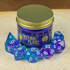 May include: A set of blue and purple polyhedral dice, alongside a jar. The jar is labelled "Astral Plane Polyhedral Dice" and has a gold lid. The dice have white numbers and are various shapes, suitable for tabletop games.