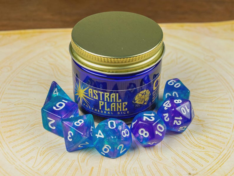 May include: A set of blue and purple polyhedral dice, alongside a jar. The jar is labelled "Astral Plane Polyhedral Dice" and has a gold lid. The dice have white numbers and are various shapes, suitable for tabletop games.