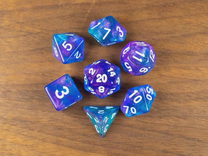 May include: A collection of seven multi-sided dice in blue and purple hues, each with white numerals. The dice are displayed on a wooden surface. These dice are designed for tabletop role-playing games.