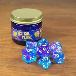 May include: A jar of blue dice with a gold lid and the text "ASTRAL PLANE POLYHEDRAL DICE". Several blue and purple polyhedral dice are scattered in front of the jar. The dice have white numbers.