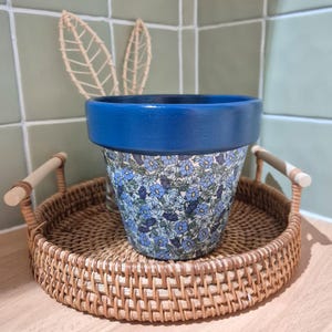 May include: A blue and white floral patterned terracotta planter with a dark blue rim, sitting on a woven wicker tray with handles.