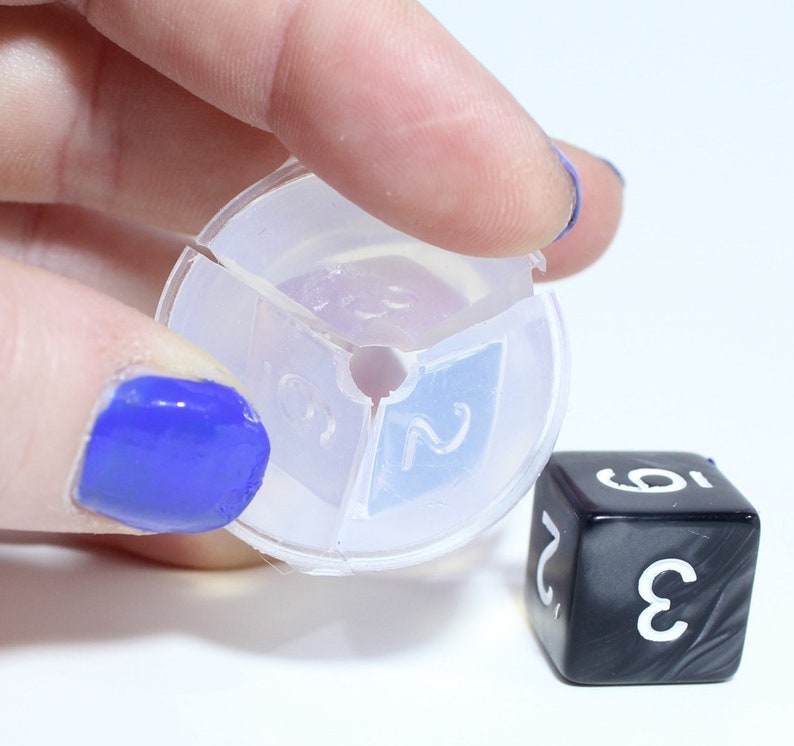 May include: A clear plastic dice rolling tray with three sections, each with a number printed on it. The numbers are 2, 3, and 5. A black dice with white numbers is sitting on a white surface.