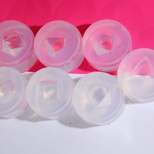 May include: Six clear silicone molds for making resin jewelry. The molds are round and have different geometric shapes inside, including a square, triangle, and diamond.