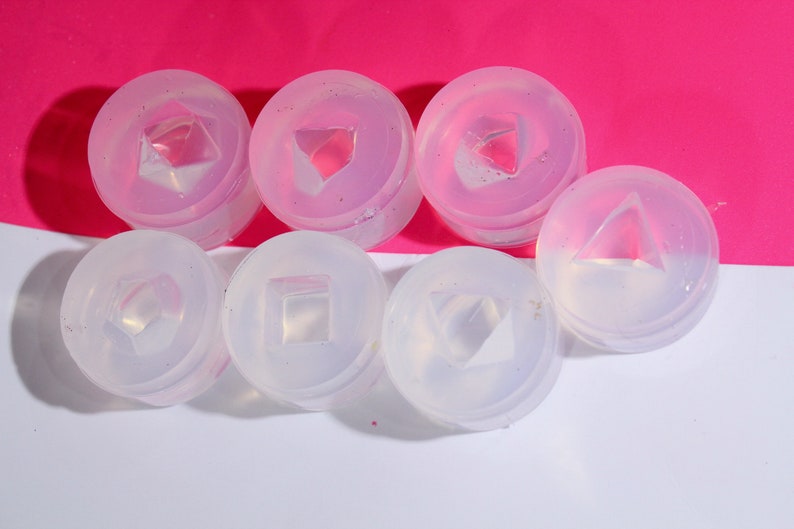 May include: Six clear silicone molds for making resin jewelry. The molds are round and have different geometric shapes inside, including a square, triangle, and diamond.