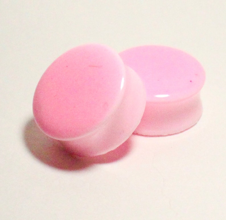 May include: Two pink acrylic ear gauges, one slightly larger than the other, with a smooth, glossy finish.
