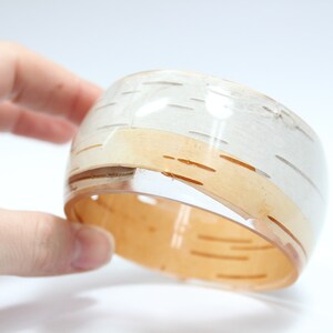 May include: A white and brown resin bangle bracelet with a birch bark pattern. The bracelet is clear and has a glossy finish.