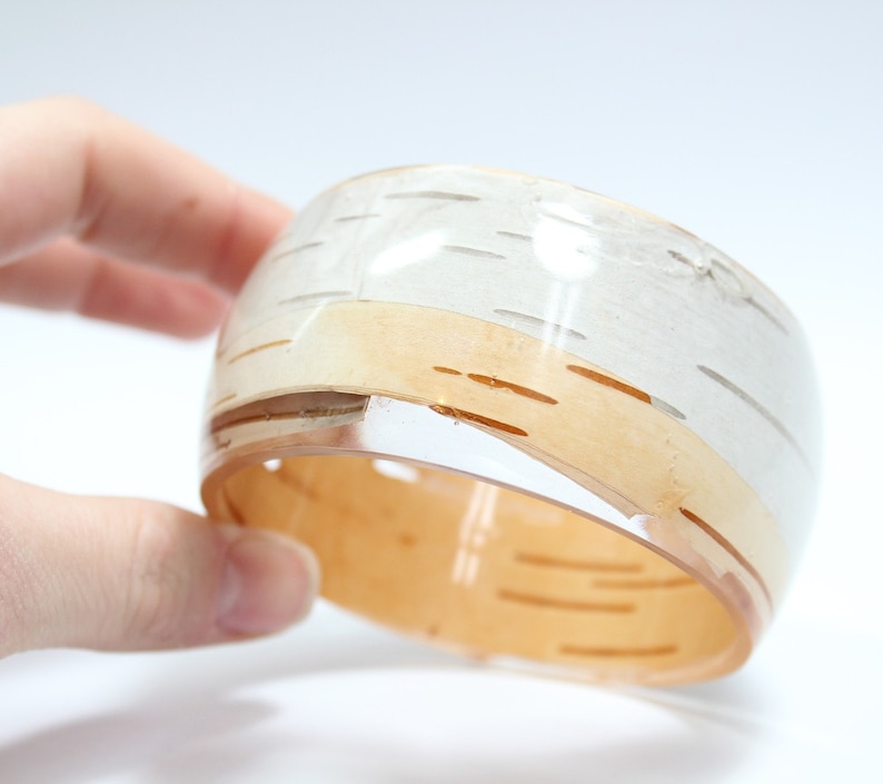 May include: A white and brown resin bangle bracelet with a birch bark pattern. The bracelet is clear and has a glossy finish.