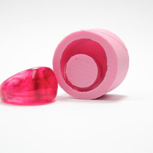 May include: Pink silicone mould for making resin rings. The mould has a round shape with a smaller circle in the centre. A pink resin ring is shown next to the mould.
