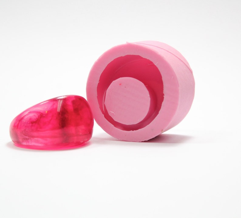 May include: Pink silicone mould for making resin rings. The mould has a round shape with a smaller circle in the centre. A pink resin ring is shown next to the mould.