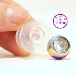May include: A clear plastic mould for making round beads, next to a finished iridescent bead with a rainbow effect. The mould is designed to create a hole in the centre of the bead. The text "Clone Mold" is visible in the image.