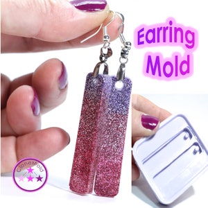 Può includere: Orecchini sfumati rossi e viola con glitter e ganci color argento. Gli orecchini rettangolari sono mostrati con uno stampo per orecchini. Il testo "Earring Mold" è anch'esso visibile.