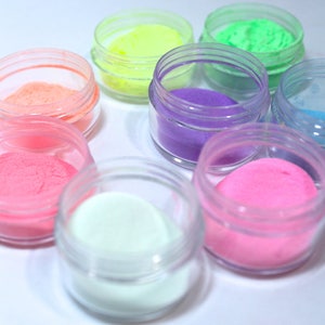 May include: Eight small jars of colorful glitter powder. The jars are clear plastic and the glitter is in various shades of pink, purple, green, blue, and white.