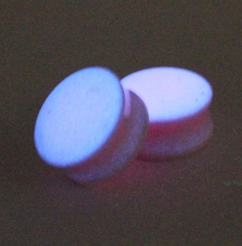 May include: Two round, white, glow-in-the-dark ear gauges. The gauges are slightly translucent and have a purple hue.