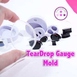 May include: A set of silicone molds for making teardrop-shaped ear gauges. The molds are purple and come with a clear plastic sheet. The image also shows several black teardrop-shaped ear gauges made with the molds. The text "TearDrop Gauge Mold" is written in pink letters.