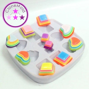 May include: A silicone mold with various colorful, layered shapes. The shapes include squares and heart-like designs in shades of blue, pink, yellow, orange, and green. The mold has the text "CloneMold" in a circle.