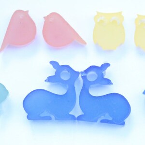 May include: A collection of colorful animal-shaped resin charms. The charms include pigs, birds, owls, rabbits, llamas, deer, and squirrels. The charms are in shades of pink, orange, yellow, purple, blue, and teal.