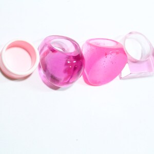 May include: Four pink plastic rings, one is a simple circle, the other three are more elaborate and have a rounded, almost heart-shaped design.