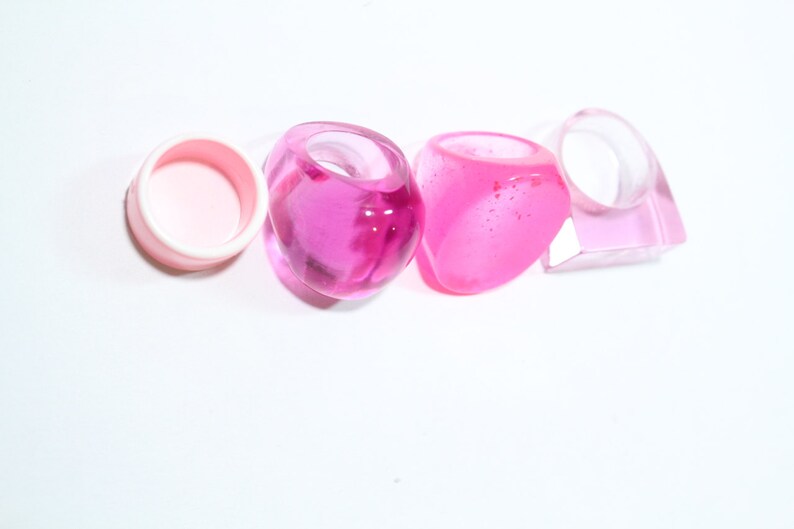 May include: Four pink plastic rings, one is a simple circle, the other three are more elaborate and have a rounded, almost heart-shaped design.