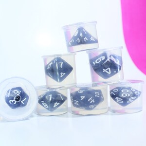May include: Six clear plastic containers with black and white dice inside. The dice are different shapes and sizes. The containers are stacked on top of each other.