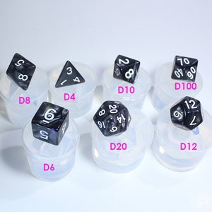 May include: A set of ten black and white dice in various shapes and sizes, including a D4, D6, D8, D10, D12, and D20. Each die is sitting in a clear plastic mold.