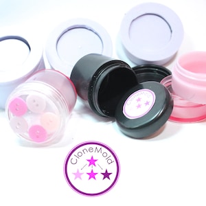 May include: A collection of small containers in various colours, including clear, pink, and black, some with lids. One container is filled with pink buttons. The black container has a lid with a pink and white "CloneMold" logo.