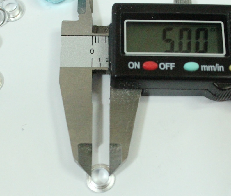 May include: A close-up of a silver metal rivet with a digital caliper measuring 5.00 mm. The caliper is black with a digital display and buttons labeled "ON", "OFF", and "mm/in".