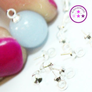 Peut inclure: Gros plan sur des fermoirs de boucles d'oreilles argentés avec une boucle en haut. Les fermoirs sont éparpillés sur une surface blanche. Une perle de verre bleu clair avec une boucle argentée est tenue par des doigts en arrière-plan. L'image comprend le texte "Clone Mold" avec trois étoiles.